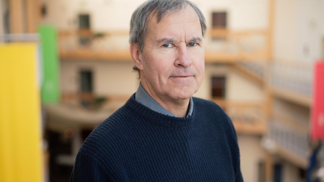 A man with grey hair, dark blue sweater and dark grey shirt. 